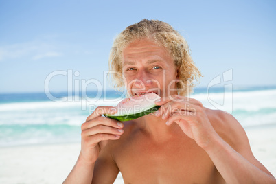 Young man eating a piece of watermelon in front of the sea