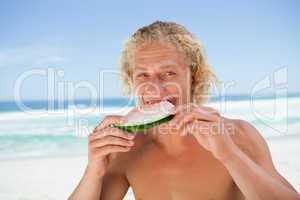 Young man eating a piece of watermelon in front of the sea