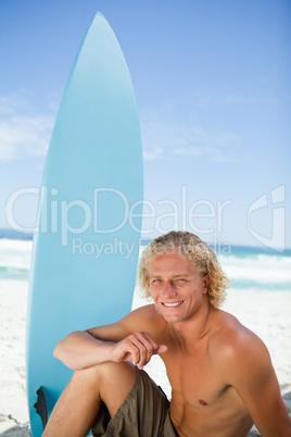 Smiling man sitting on the beach with his arm on his leg