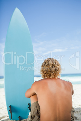 Blonde man sitting on the beach with his arms around his legs