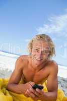 Smiling blonde man sending a text while sunbathing on the beach