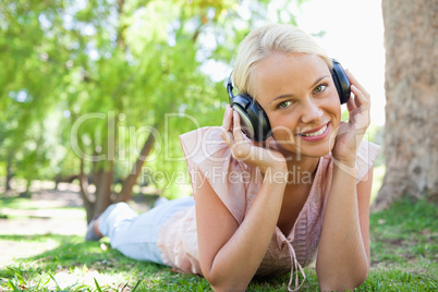 Smiling woman listening to music while lying on the lawn