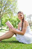 Side view of a smiling woman sitting on the grass with a book