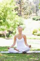 Smiling woman sitting in a yoga position in the park