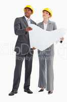 Businessman and woman wearing hard hats holding paper looking up