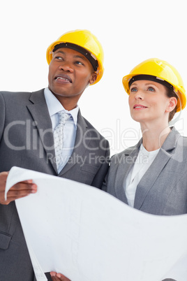 Smiling business people wearing hard hats are holding a paper