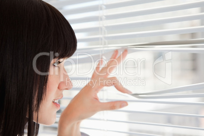 A young woman looking out through window blinds