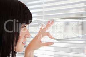 A young woman looking out through window blinds