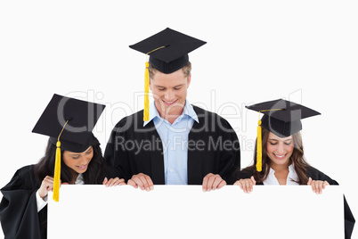 Three students having graduated holding blank sheet and looking