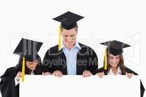 Three students having graduated holding blank sheet and looking