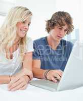 A smiling couple sitting and using the laptop