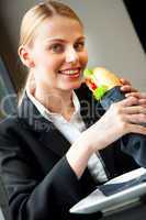young smiling businesswoman eating a sandwich and looking at cam