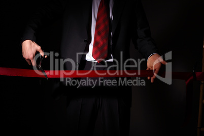 Businessman with scissors cuting a red ribbon