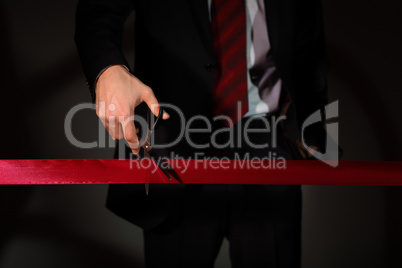 Businessman with scissors cuting a red ribbon