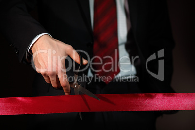 Businessman with scissors cuting a red ribbon