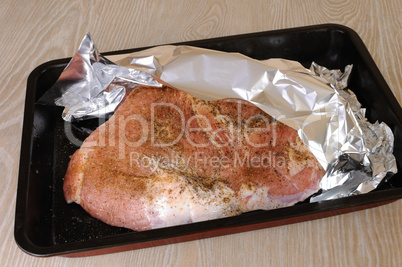 A piece of pork ham on a baking sheet under the foil