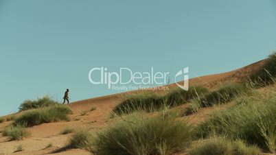 Bushman hunter walking up a dune