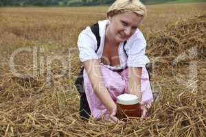Frau im Dirndl kniet mit Bierglas in einem Feld