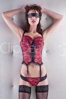 Blindfold seductive woman in a corset and stockings standing in