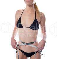 Beautiful young woman in bikini measuring waist