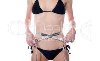 Sensual female measuring her waist size with tape
