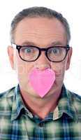 Surprised aged male with paper heart over his mouth