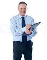 A smiling ethnic businessman writing on a clipboard folder