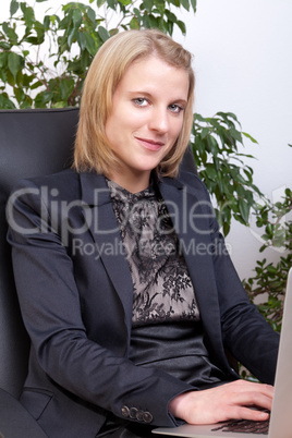 Junge Geschäftsfrau mit Notebook auf den Knien lächelt in die Kamera