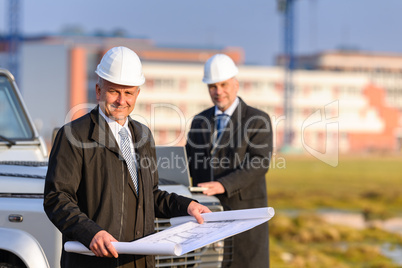 Two architects at construction site review plans