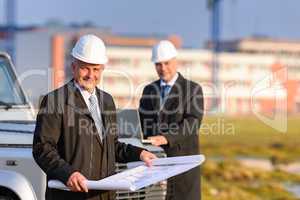 Two architects at construction site review plans