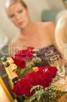 Pensive Blonde Sits at Mirror Near Champagne and Roses