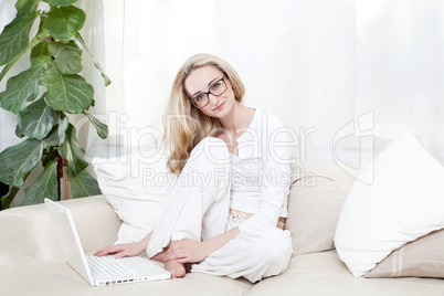 Junge Frau sitzt mit einem Laptop unter einem Fenster auf einer