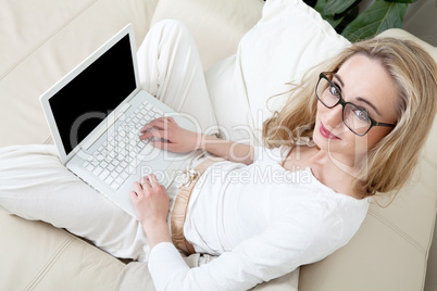 Junge Frau sitzt mit einem Laptop unter einem Fenster auf einer
