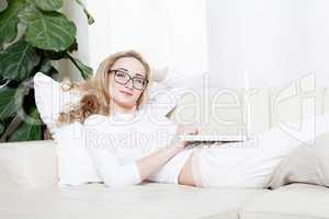Junge Frau liegt mit einem Laptop unter einem Fenster auf einer