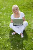 Blonde woman using a laptop on the grass