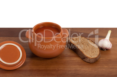 Soup in ceramic pot with bread and garlic