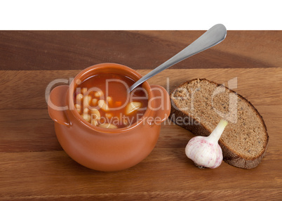 Soup in ceramic pot with bread and garlic on wooden table