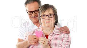 Old couple facing camera with focus on paper heart