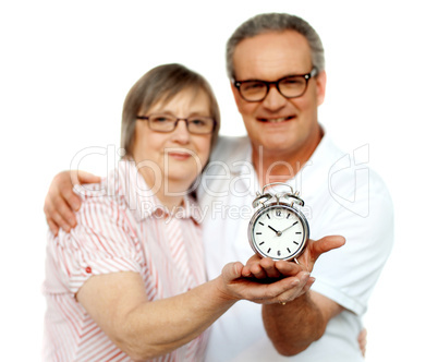 Aged couple with alarm clock on plam