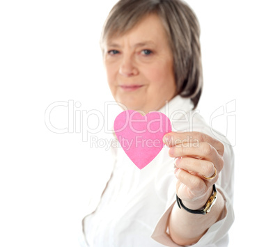 Focus on pink paper heart. Aged woman holding it