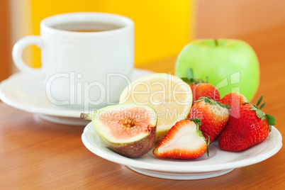 cup of tea, apple, lemon, fig and strawberries on a plate