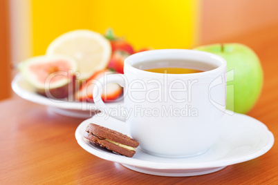cup of tea,cookie,apple, lemon, fig and strawberries on a plate