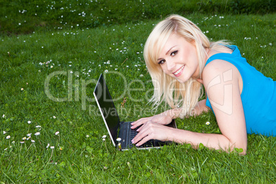 Smiling woman using her laptop on the grass