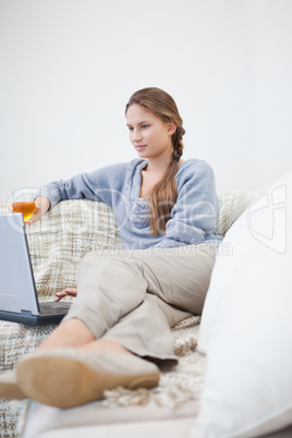 Women sitting and holding a glass while typing on a laptop