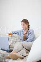 Woman sitting and holding a glass while looking on a laptop