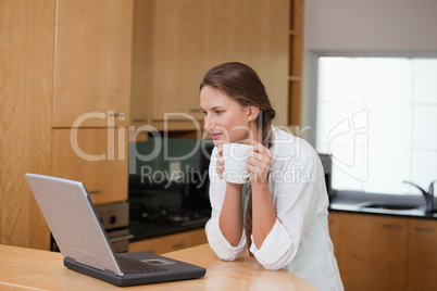 Woman looking at a computer while holding a cup