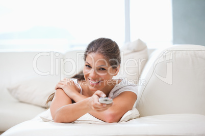 Woman lying on a sofa while pointing with a remote