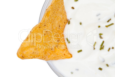 A nacho dipped into a bowl of white dip with herbs