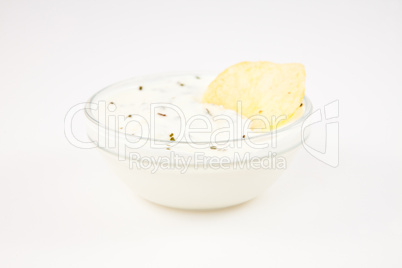 Bowl of dip with herbs with a chip dipped in it