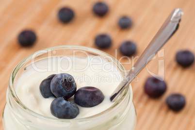 Close up of a pot of yoghurt with blueberries displayed behind